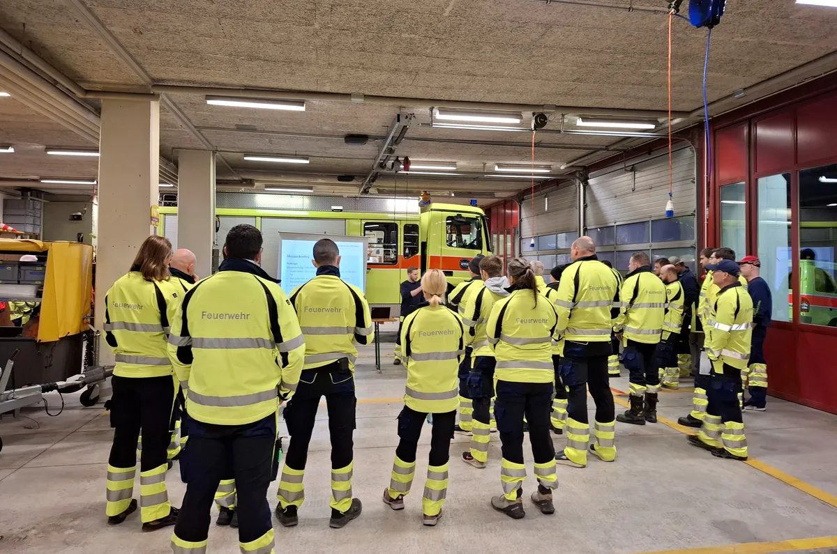 Vor der Grossübung fand noch ein Briefing für die Feuerwehrleute statt.none Mehrere Menschen stehen vor einer Leinwand im Depot der Feuerwehr.